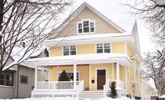 a yellow house with white trim and snow on the ground in front of it is surrounded by trees