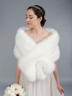 a woman in a white dress holding a bouquet and wearing a fur stole over her shoulders