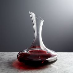 a glass vase sitting on top of a white table next to a red liquid bottle