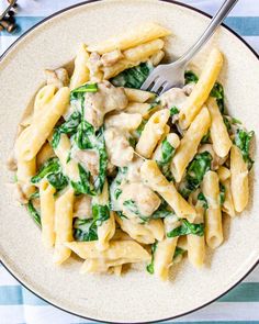 a white plate topped with pasta covered in sauce and spinach next to a fork