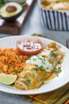 a white plate topped with rice and enchilada next to a bowl of salsa