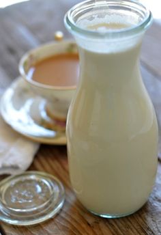 a bottle of milk sitting on top of a wooden table next to a cup of coffee