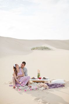 a man and woman sitting on top of a blanket in the desert