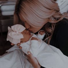 a woman holding a baby in her arms and kissing it's face with a big bow on its head