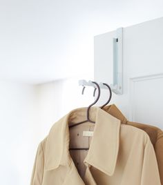 a coat hanging on a hook in front of a white door with an open jacket hanger