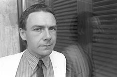 a man wearing a suit and tie standing in front of a window