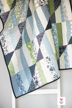 a blue and green patchwork quilt hanging on a white chair next to a wall