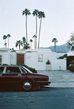 a red car parked in front of a white house with palm trees on the side