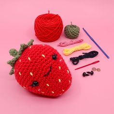 a crocheted strawberry is sitting next to some knitting supplies on a pink surface