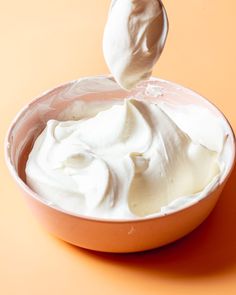 a spoon full of whipped cream sitting in a bowl on an orange surface with a white background