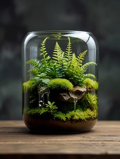 a glass jar filled with plants and moss on top of a wooden table next to a window