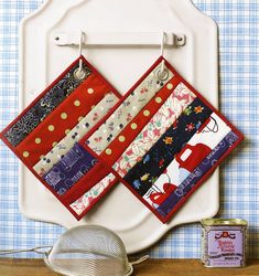 two quilted pot holders hanging from hooks on a wall next to a tea strainer