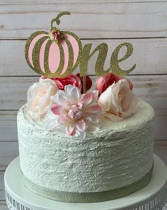 a white cake with pink and gold flowers on top is sitting on a wooden table