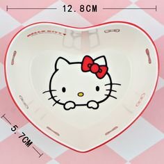 a hello kitty heart shaped dish with a bow on it's head, sitting on a checkered tablecloth