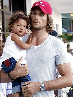 a man holding a small child while wearing a red hat and blue jeans is walking down the street