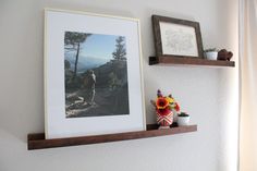 two wooden shelves with pictures and vases on them, one is holding a flower