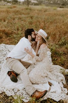 a man and woman sitting on top of a blanket in the middle of a field