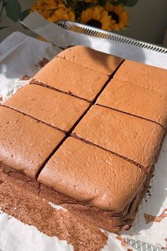 there is a cake that has been cut into squares and placed on a table with flowers in the background