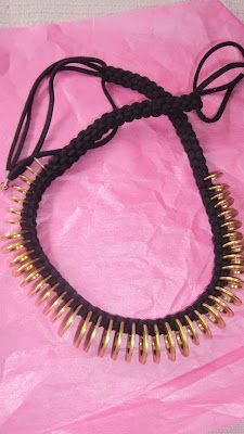 a black and gold necklace on pink paper