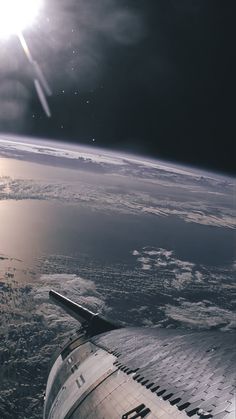 an airplane wing flying over the ocean under a cloudy sky with sun shining down on it