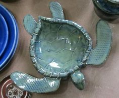 a ceramic turtle sitting on top of a table next to blue plates and utensils