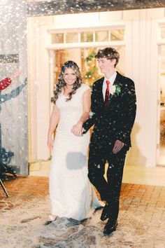 a bride and groom are walking through the snow at their wedding reception in front of a christmas tree