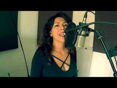 a woman singing into a microphone in front of a recording booth with an empty screen behind her