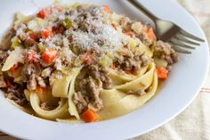 a white plate topped with pasta covered in ground beef and carrots next to a fork