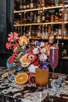 a table topped with glasses filled with liquid next to an orange slice and flower arrangement