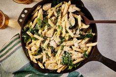 a skillet filled with pasta and spinach on top of a table next to glasses