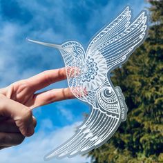 a hand is holding up a cutout of a bird in front of some trees