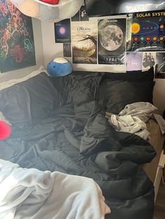 an unmade bed with black sheets and posters on the wall