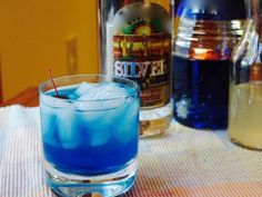 a blue drink sitting on top of a table next to two bottles of alcohol and a glass