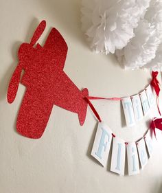 a paper airplane banner hanging on the wall next to some flowers and tissue pom poms