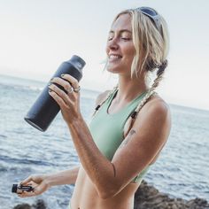 a woman holding a water bottle and looking at the ocean