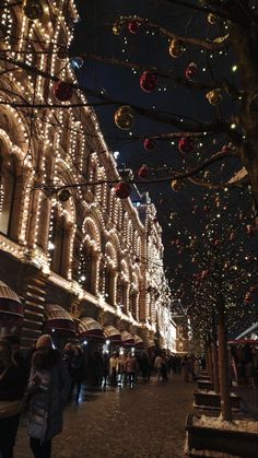 people are walking down the street under christmas lights