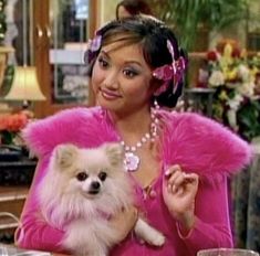 a woman sitting at a table with a small dog in her lap and wearing a pink outfit