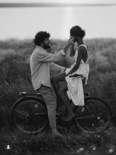 a man and woman sitting on a bike by the water with their backs to each other