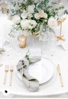 a table set with white and gold place settings, silverware, napkins and flowers