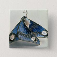 a blue butterfly brooch with pearls on it's wings and two white beads hanging from the back