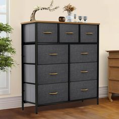 a black and grey dresser with gold handles in a room next to a potted plant