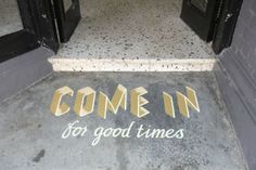 the words come in for good times are painted on the sidewalk next to some doors