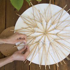 two hands are working on an umbrella made out of toothpicks and bamboo sticks