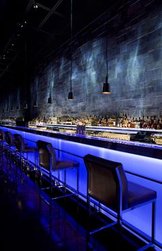 an empty bar is lit up with blue lights and black chairs in front of the bar