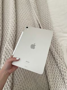 a person holding an apple ipad in their hand on top of a bed with white sheets