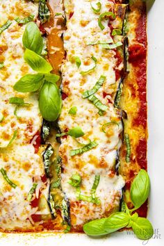 a square pizza with cheese, sauce and basil leaves on the top is ready to be eaten