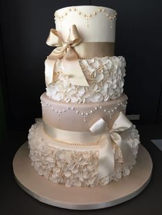 a three tiered wedding cake with white flowers and bows on the top, sitting on a platter