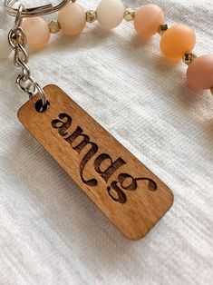 a wooden keychain with an engraved name and beaded necklace on it, along with other beads