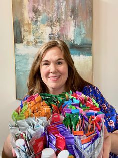 a woman holding a large basket full of crafting supplies in front of a painting