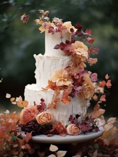 a three tiered cake with flowers and leaves on top is surrounded by fall foliage